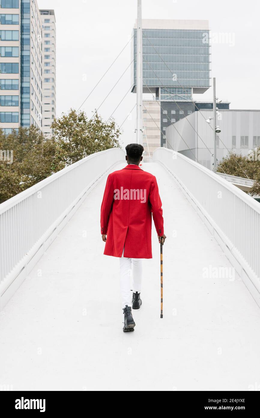 Man wearing red jacket walking with walking cane on bridge in city Stock Photo