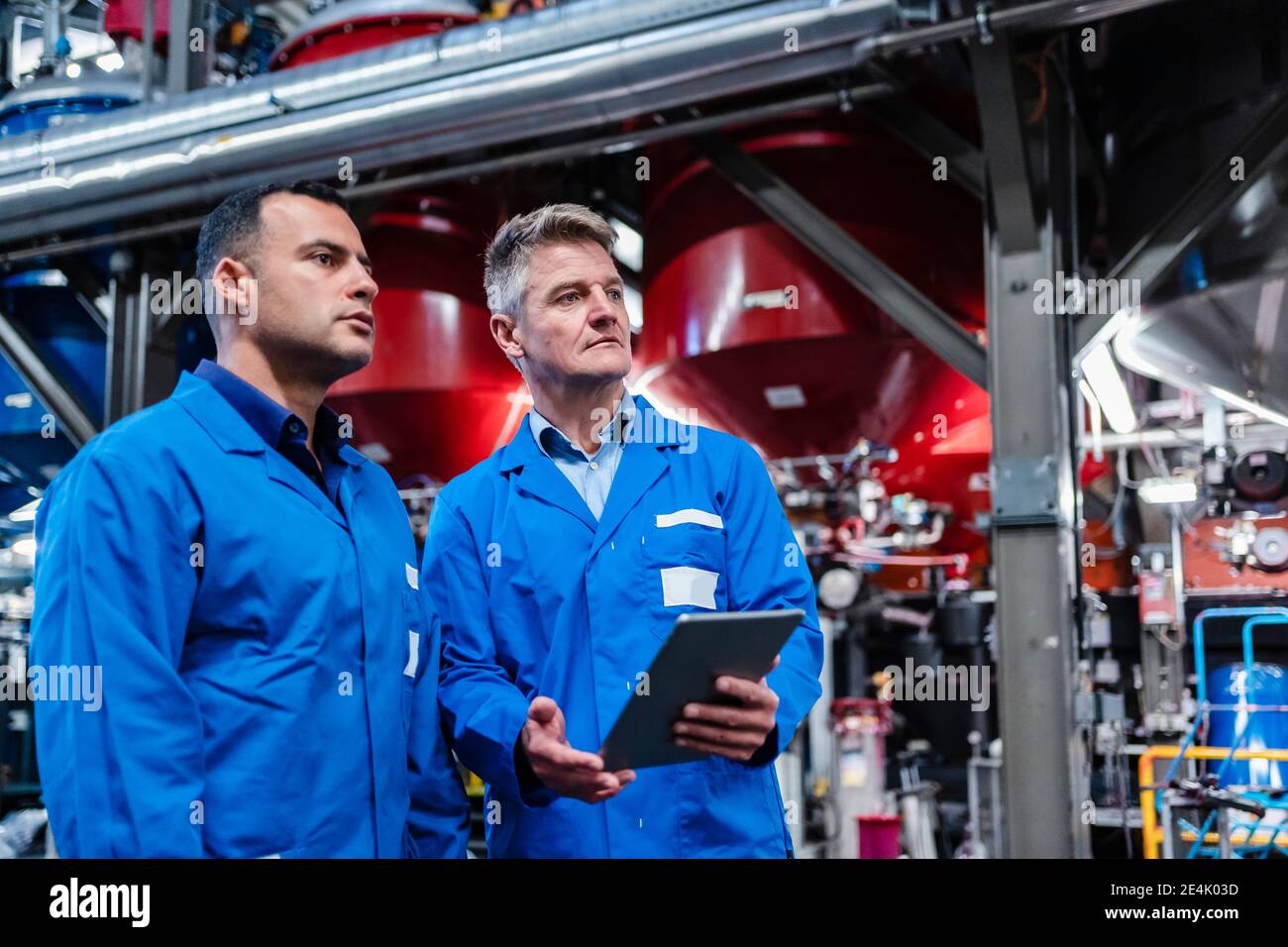 Multi ethnic technicians with digital tablet looking away while standing in industry Stock Photo