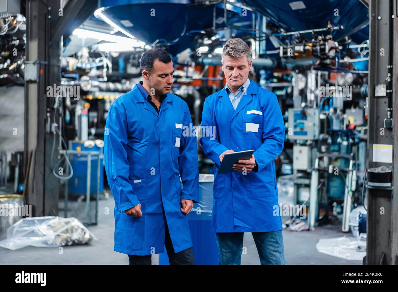 Male technicians in blue coat using digital tablet while working in industry Stock Photo
