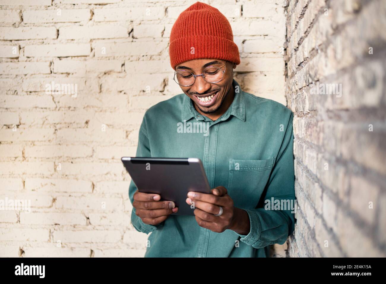 Happy man using digital tablet while leaning by brick wall Stock Photo