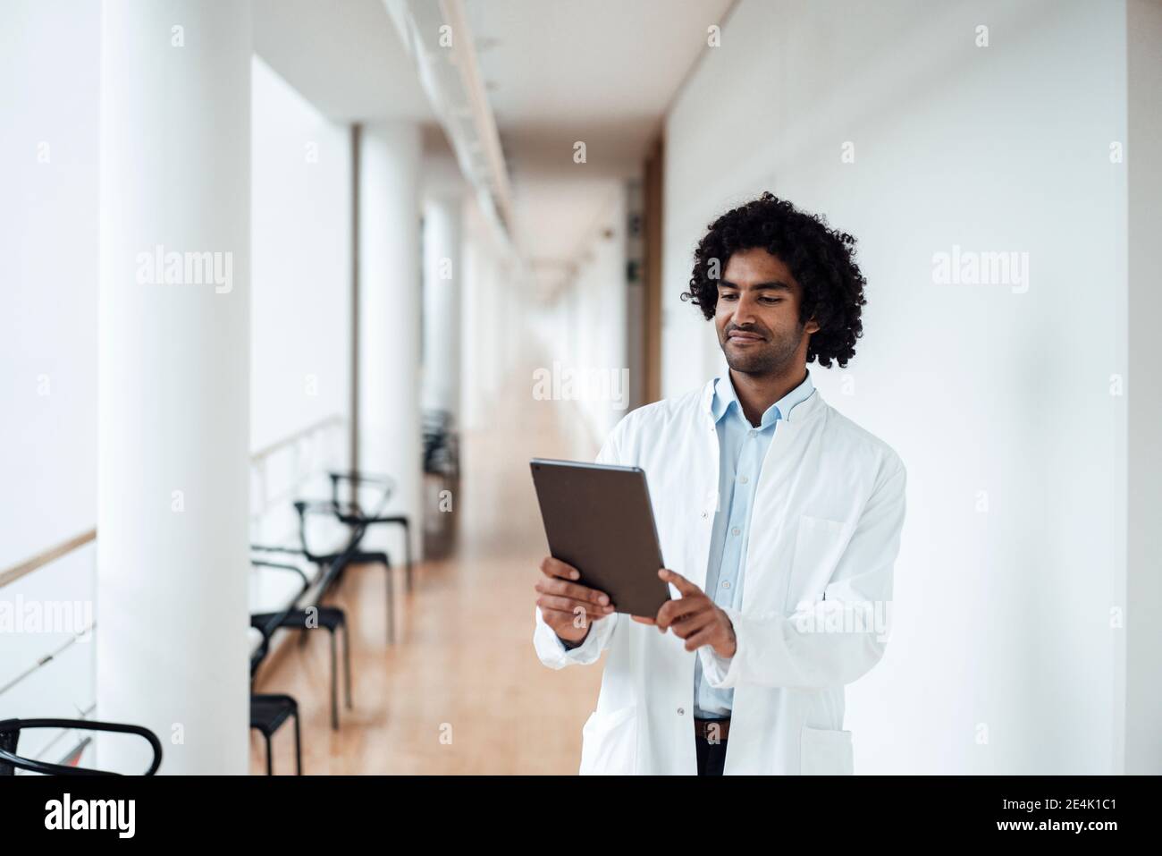 Confident young male doctor using digital tablet at hospital corridor Stock Photo