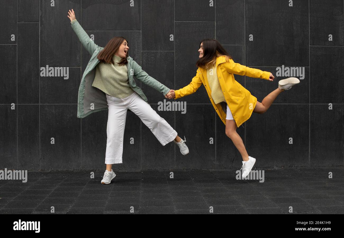 Happy sisters holding hands while running against black wall Stock ...
