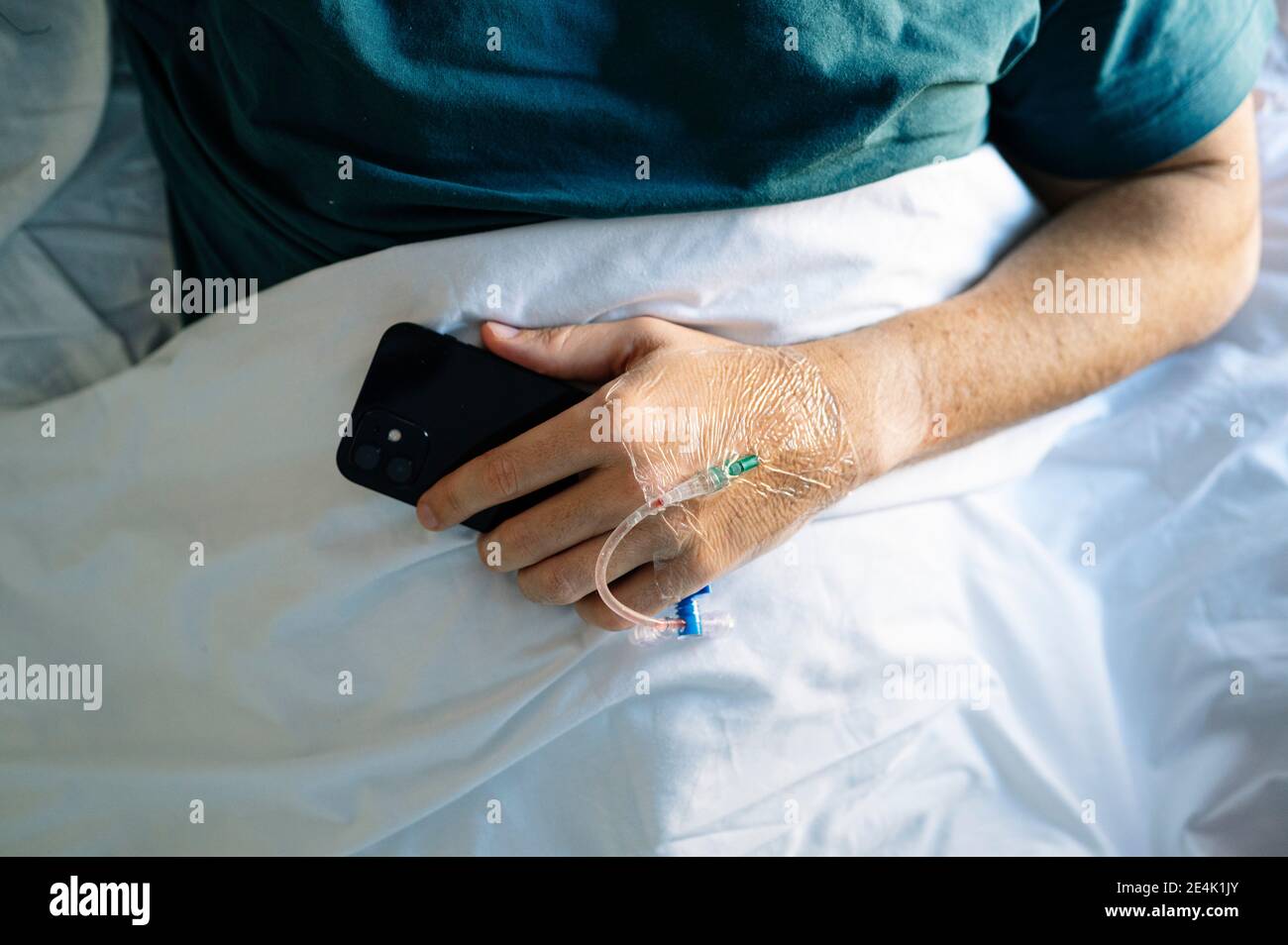 Woman removing IV drip from patient hand while standing by bed in hospital Stock Photo