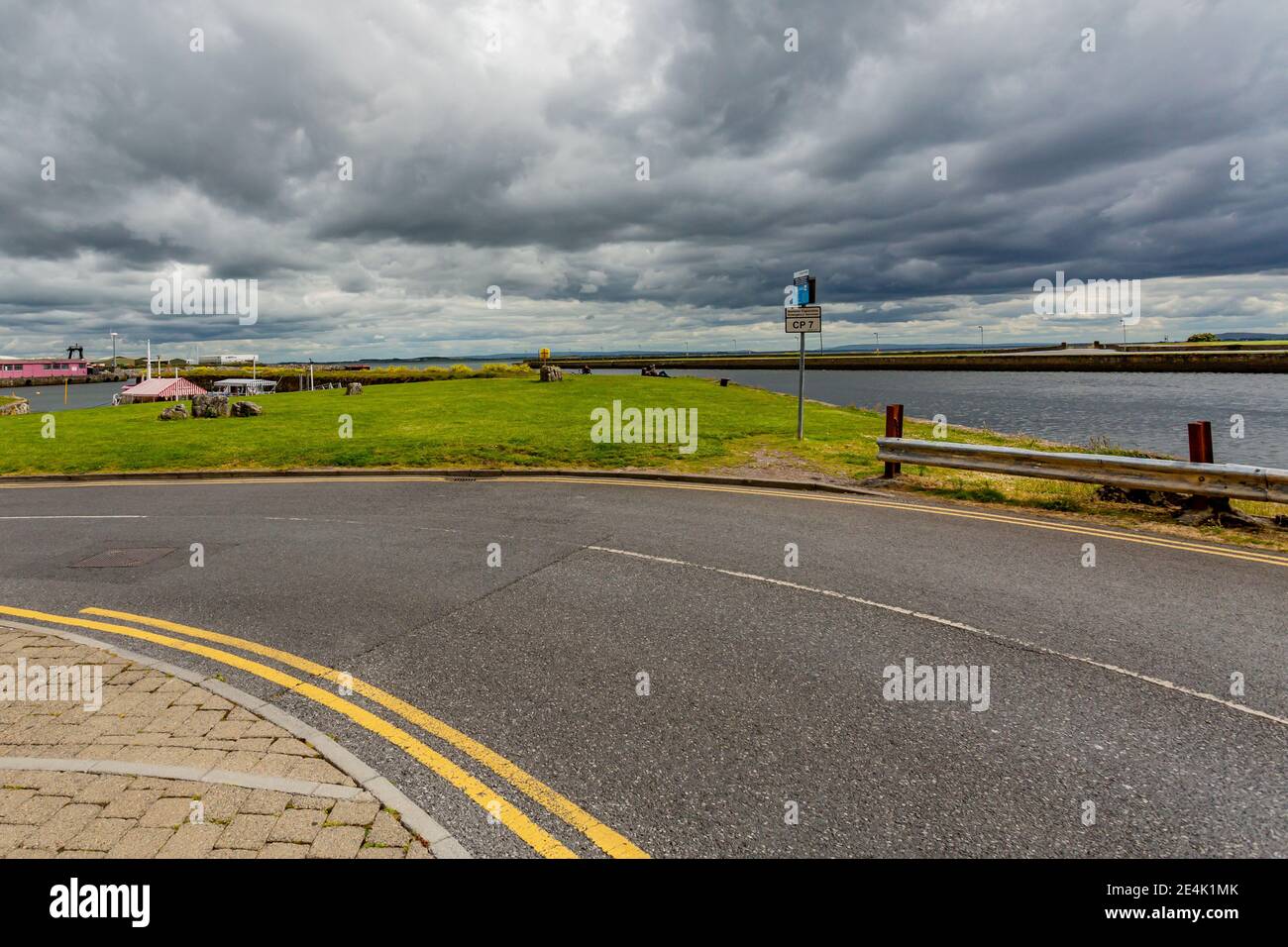 Curve in an empty street known as the Long Walk through Galway Bay, green grass with the Corrib River in the background, cloudy day with thick gray cl Stock Photo