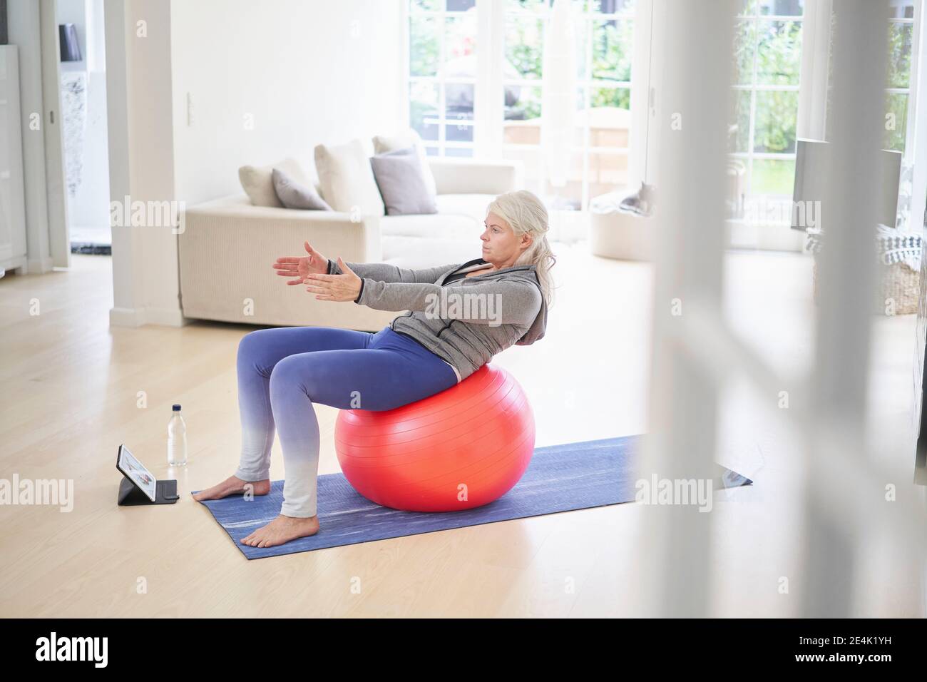 Senior woman exercising on fitness ball while learning from online tutorial through digital tablet at home Stock Photo