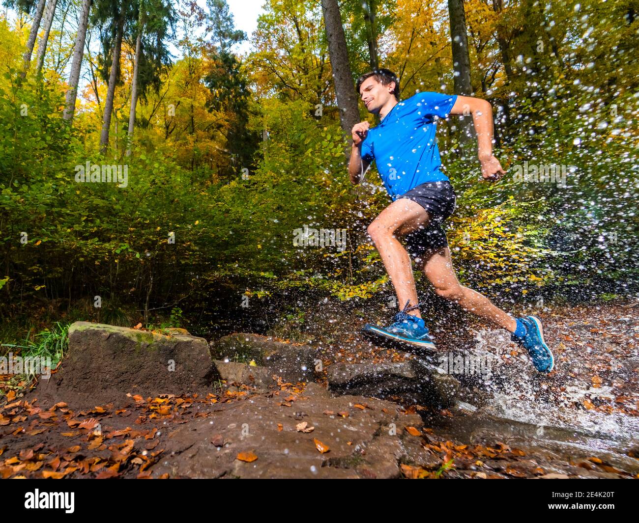 Young male sportsperson splashing water while trail running in autumn forest at Kappelberg, Germany Stock Photo