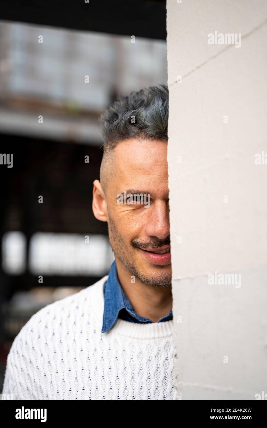 Smiling man hiding behind wall Stock Photo