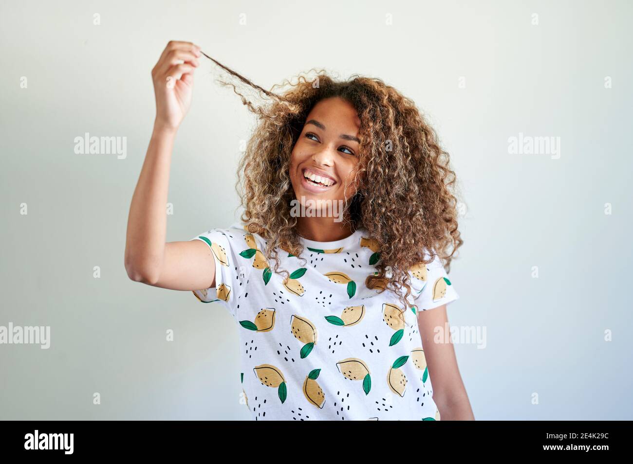 Smiling young woman looking at her hair against white wall Stock Photo