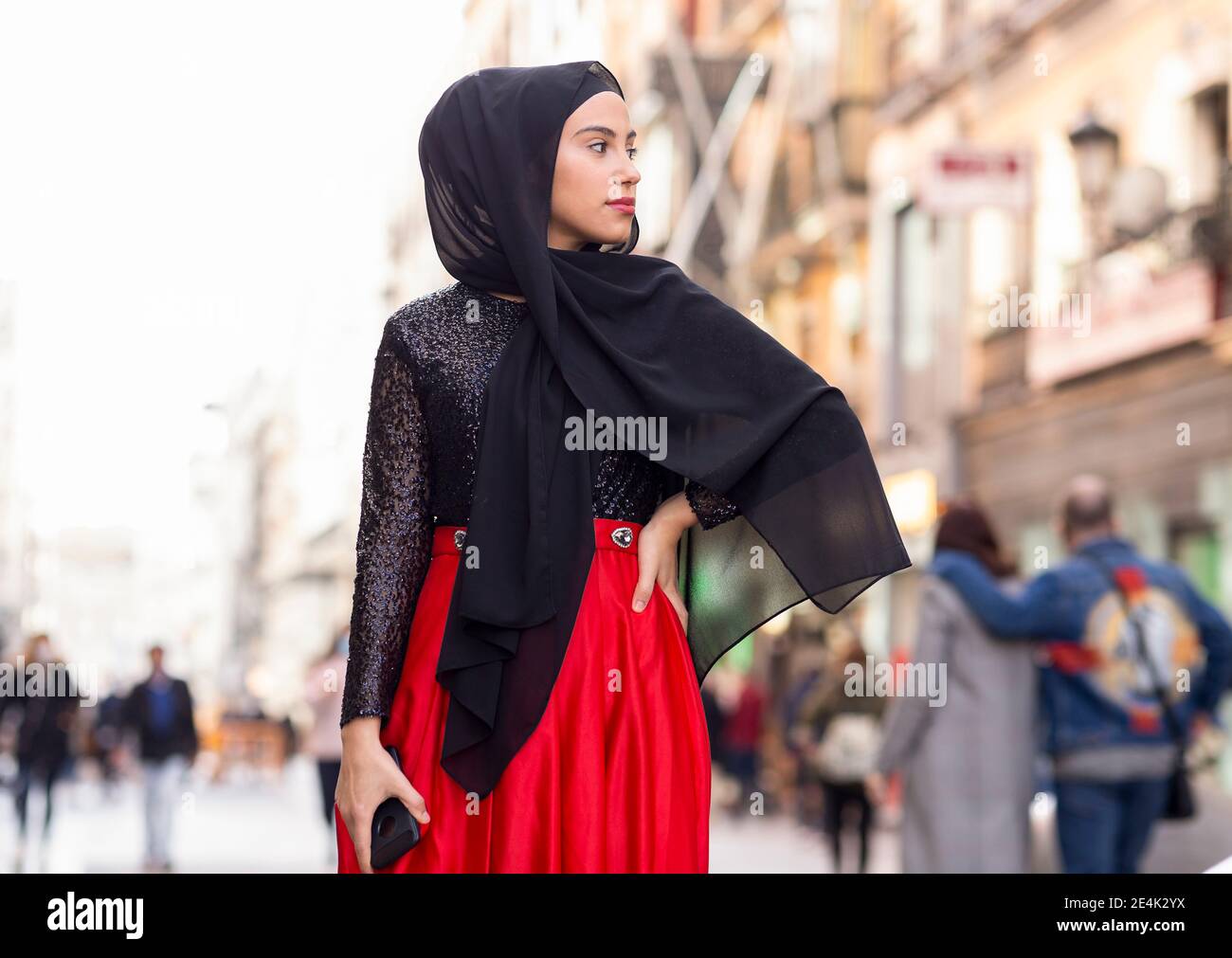 Portrait of young woman wearing black hijab posing outdoors with hand on hip Stock Photo