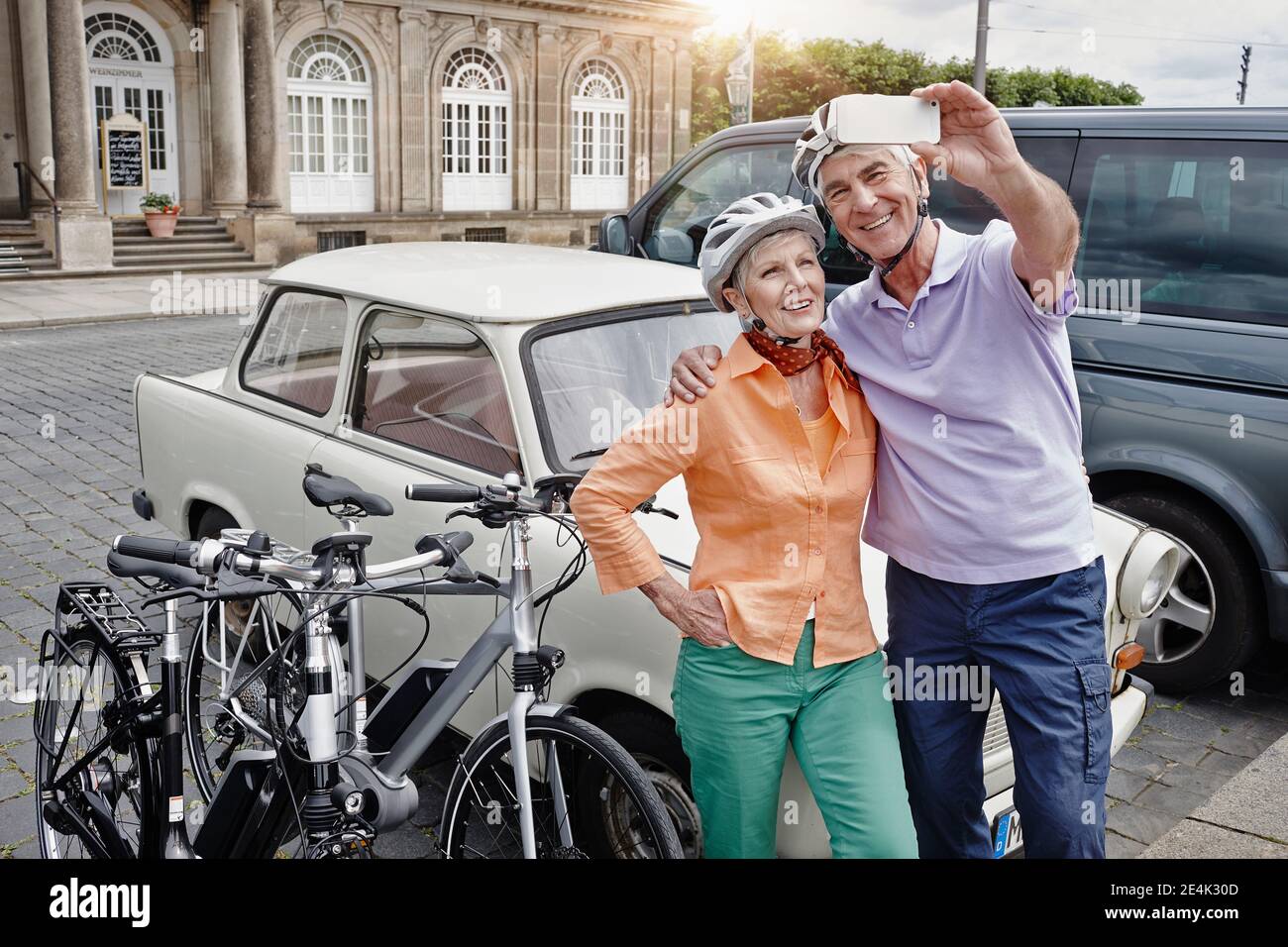 Smiling couple wearing cycling helmet taking selfie Trabant car while standing at Dresden, Germany Stock Photo