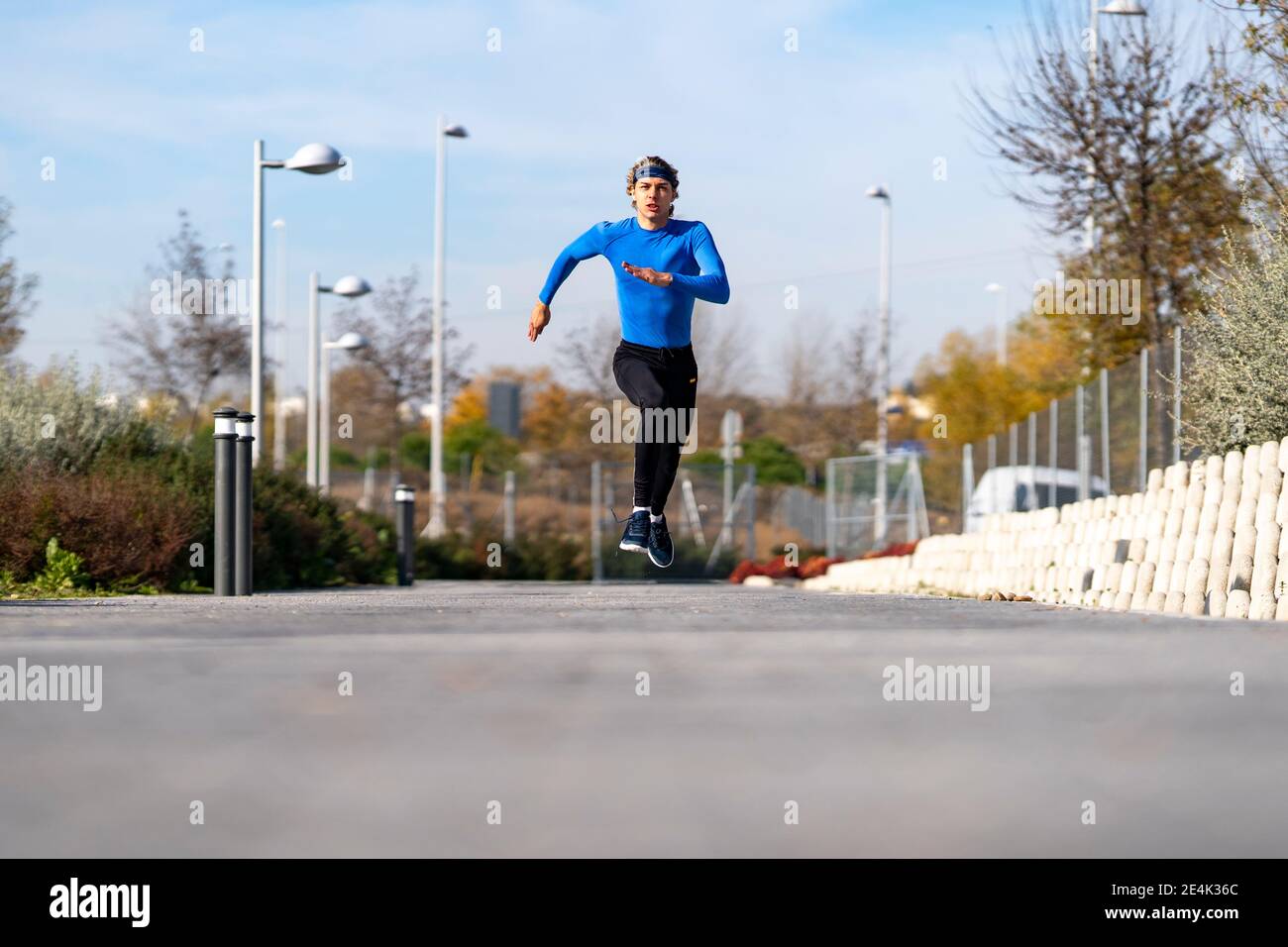 Sportsman running with dedication on footpath in public park on sunny day Stock Photo