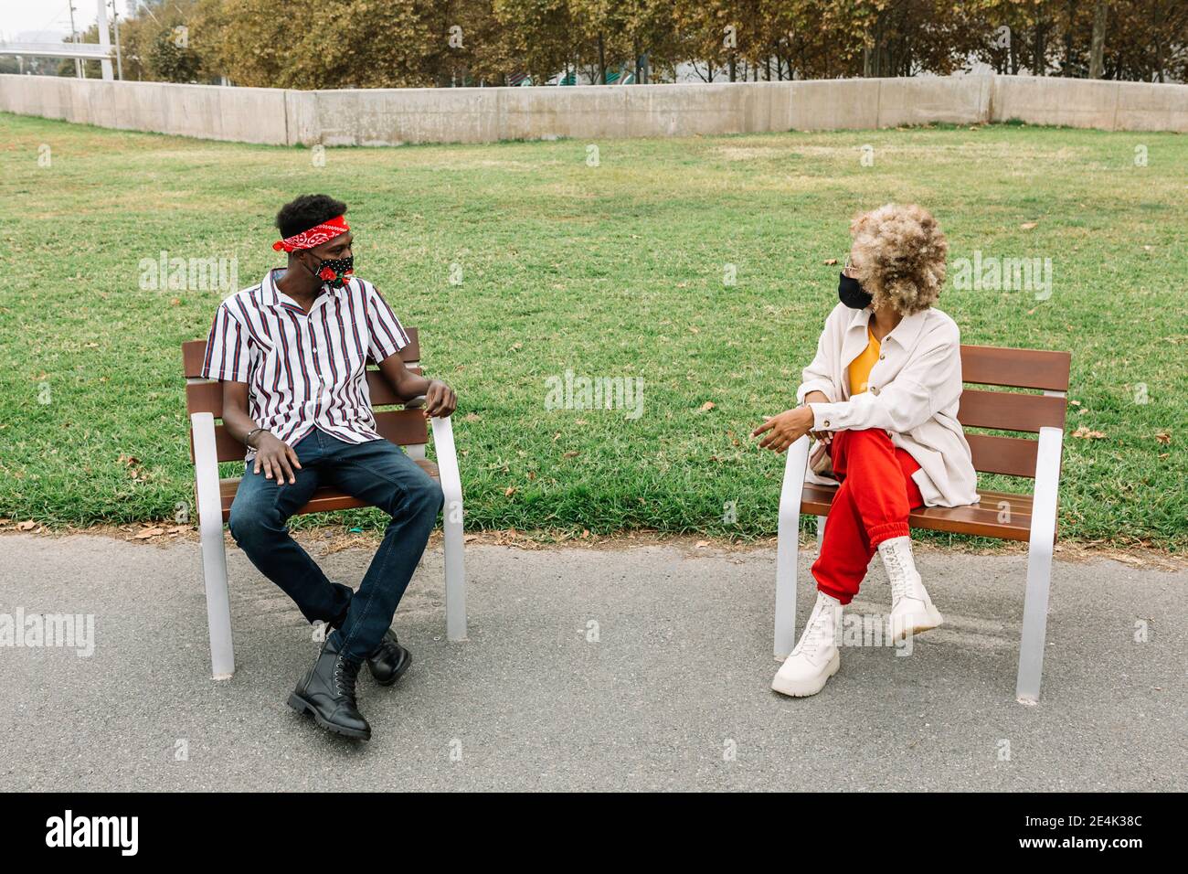 Friends wearing face mask talking while sitting on chair with social distance Stock Photo