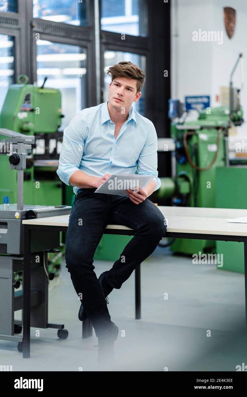 Male engineer with document looking away while siting on desk in industry Stock Photo