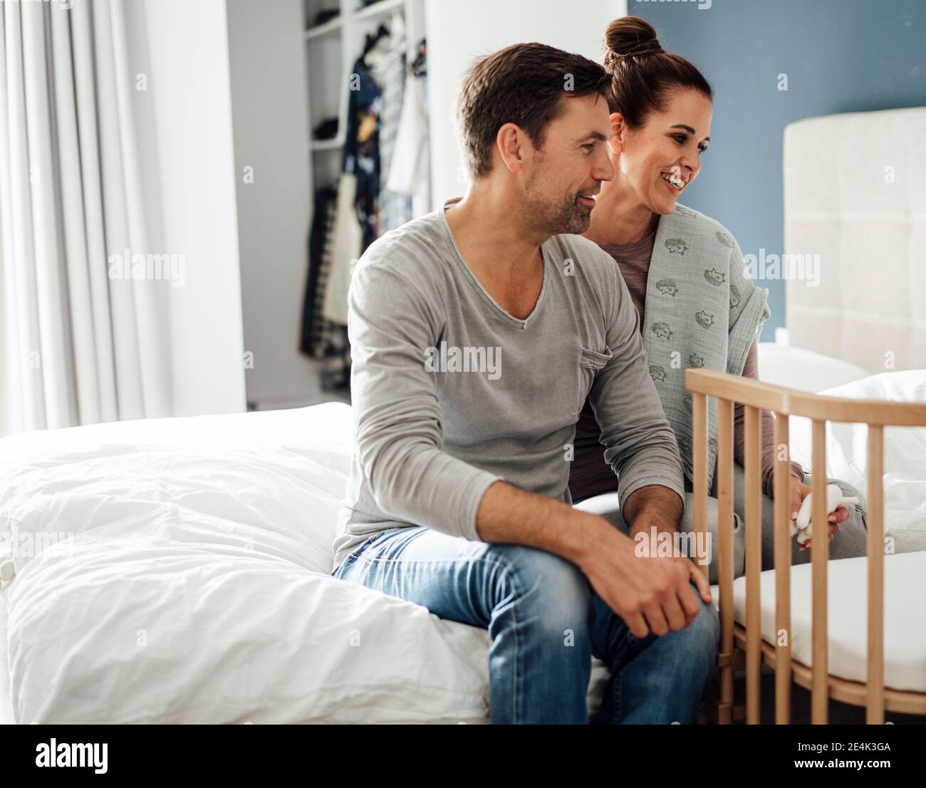 Smiling mature couple admiring crib while sitting on bed at home Stock Photo