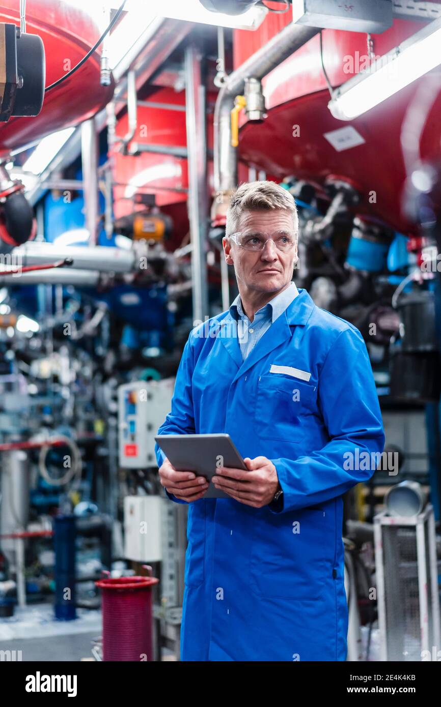 Mature engineer looking away while holding digital tablet in factory Stock Photo