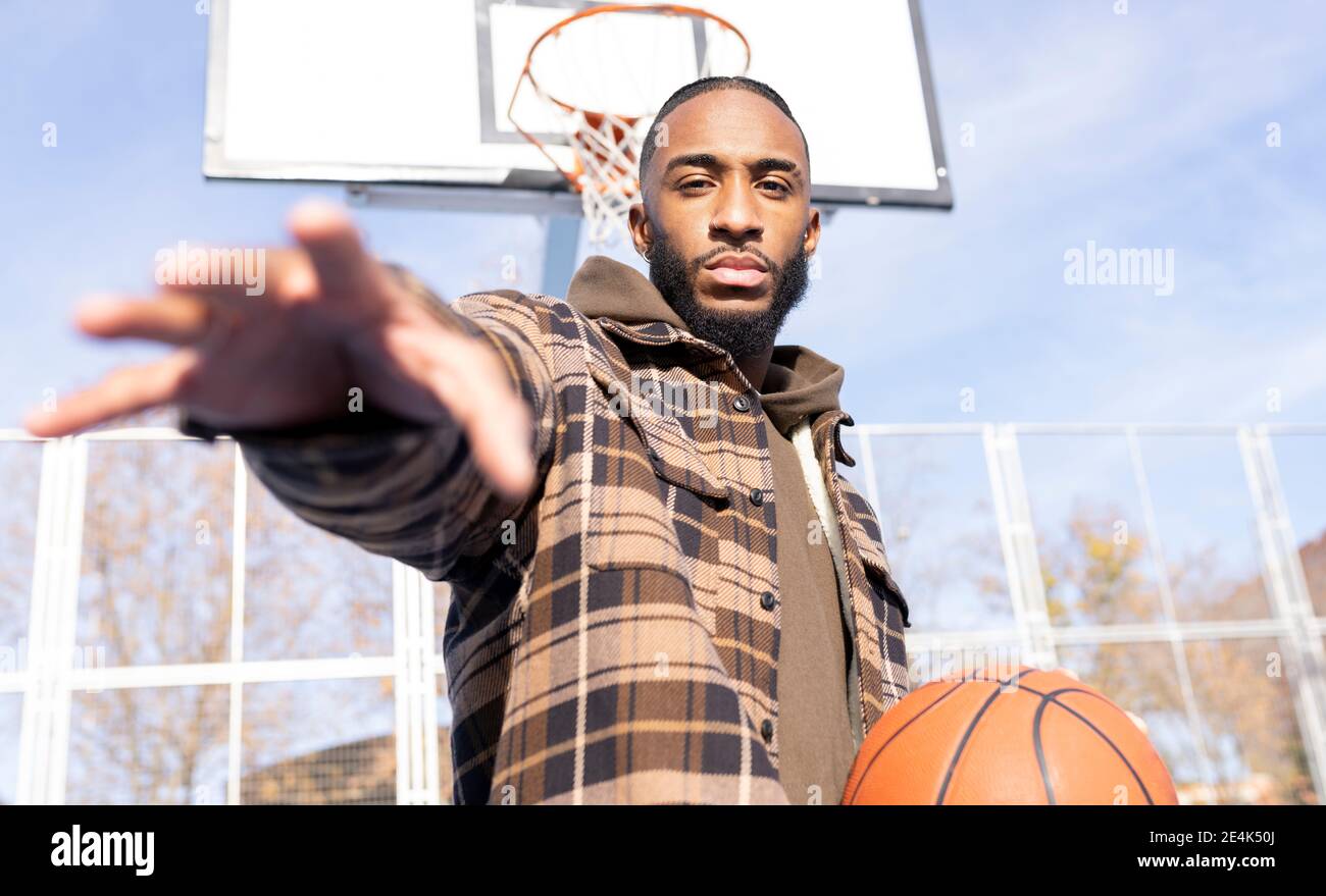 Young boy gesturing while holding basketball in court on sunny day Stock Photo