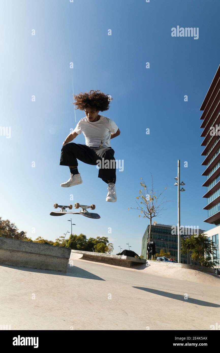 Young sportsman practicing kickflip with skateboard on sunny day Stock Photo