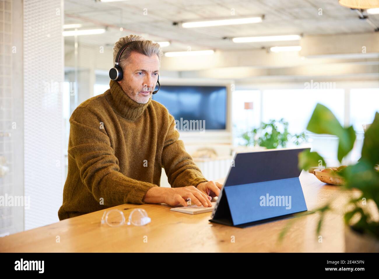 Businessman wearing headset talking while working on digital tablet at office Stock Photo