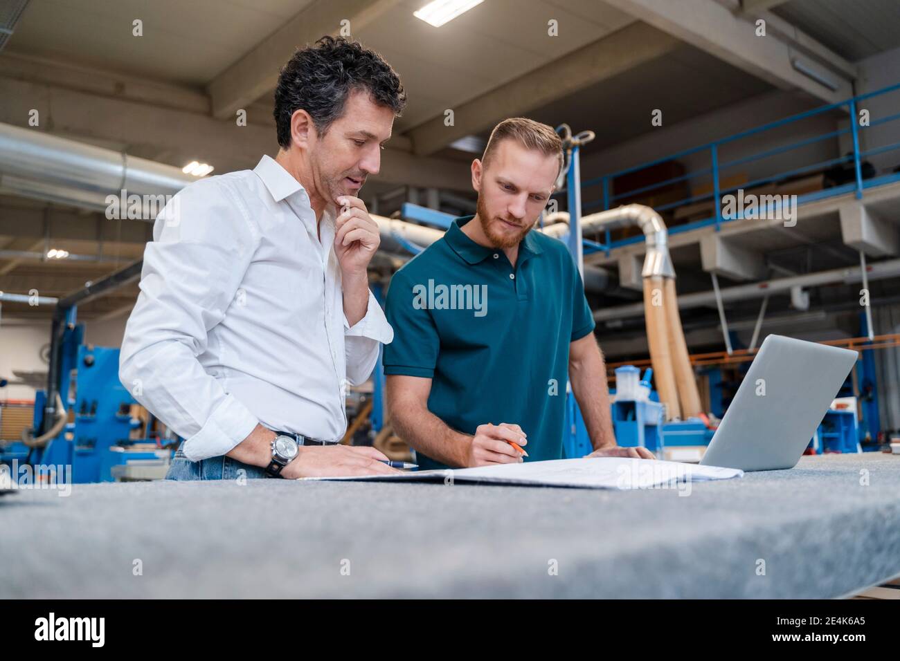 Two carpenters talking over documents in production hall Stock Photo