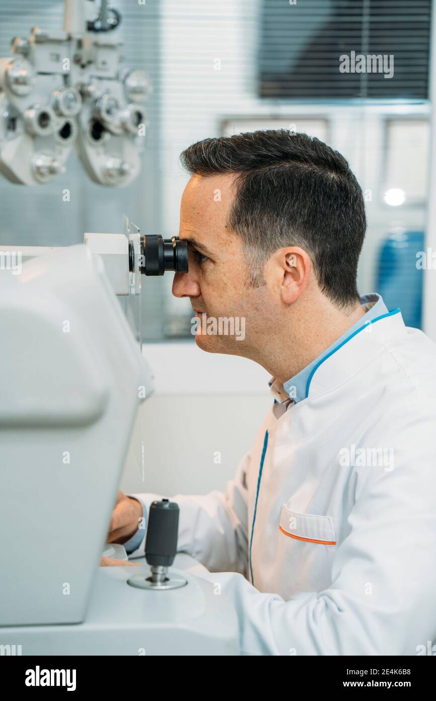 Male optometrist looking phoropter in clinic Stock Photo