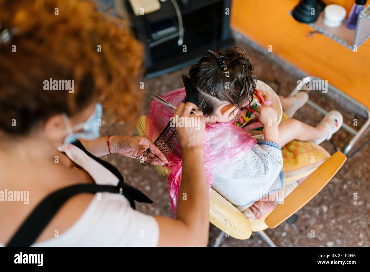 Hairdresser cutting wet hair of flittle girl searching clips in basket Stock Photo