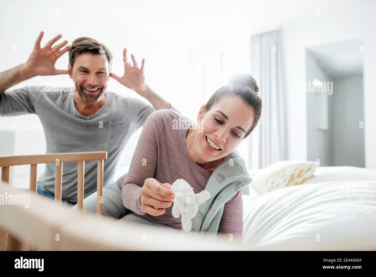 Playful mature couple sitting by crib on bed at home Stock Photo