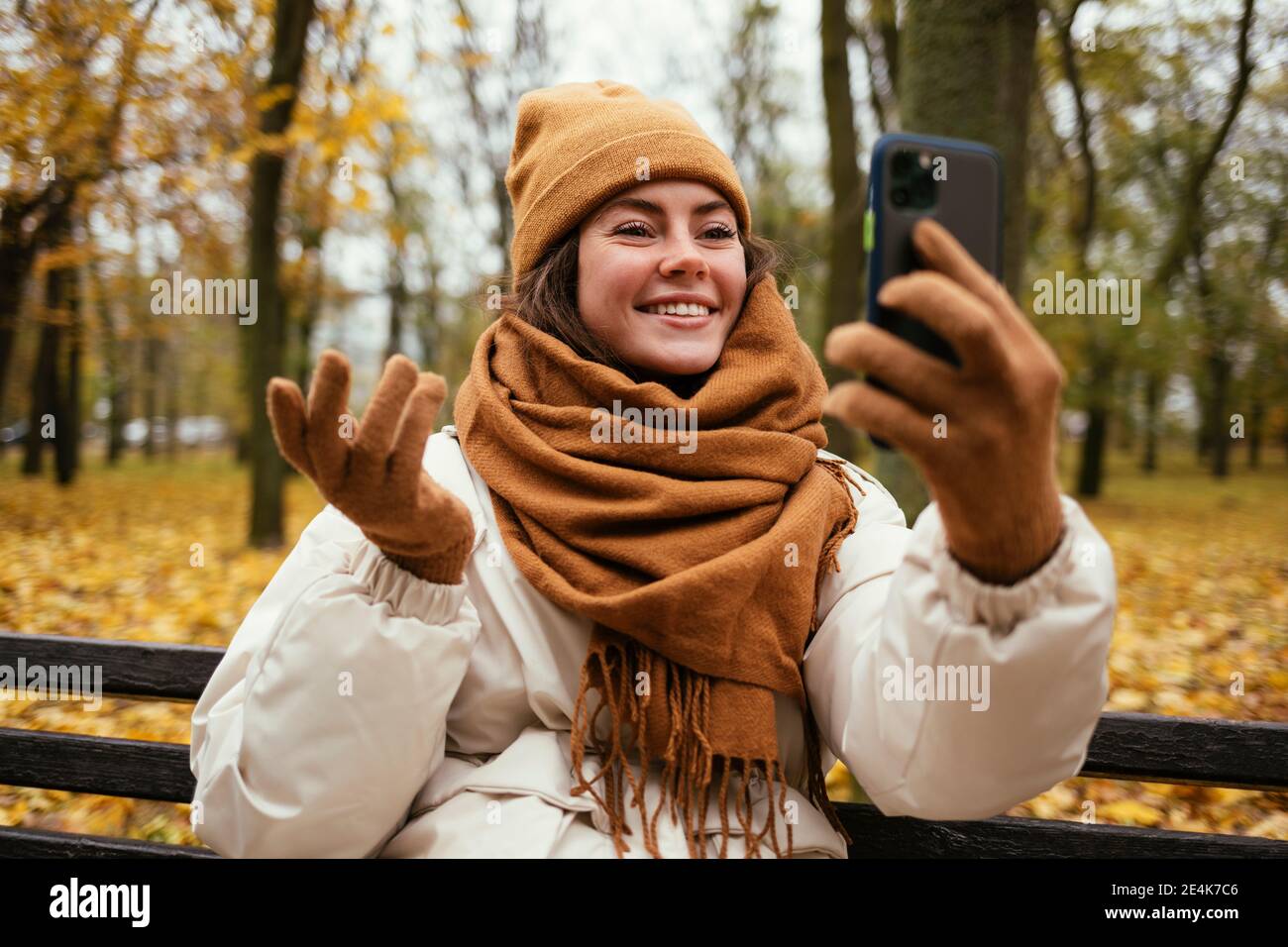 Smiling young woman hand gesturing while talking on video call in autumn park Stock Photo
