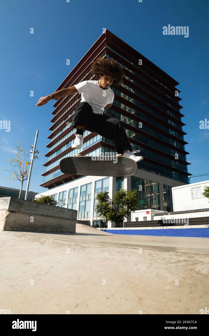 Man practicing kickflip with skateboard while jumping at skateboard park Stock Photo