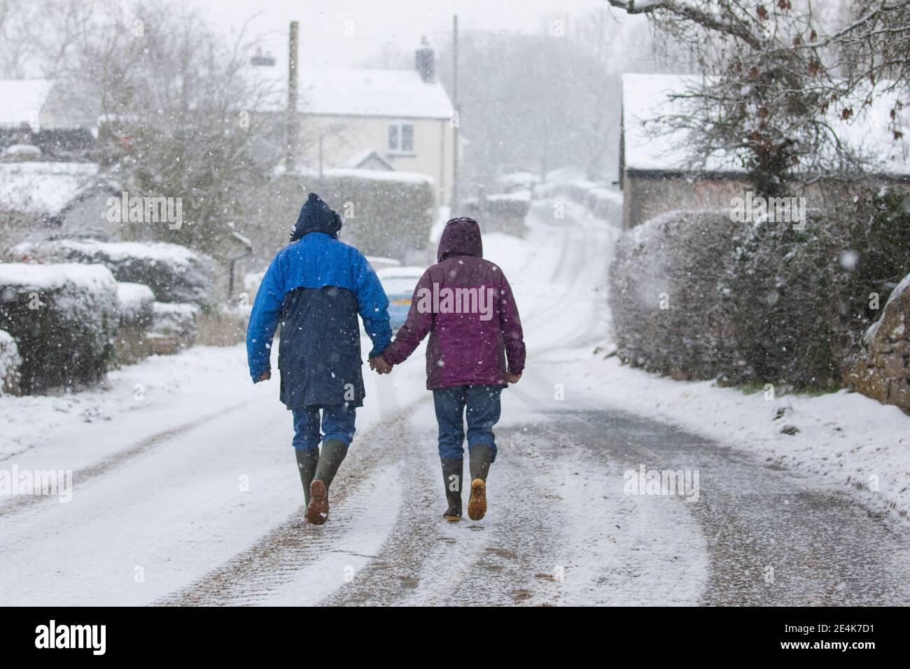 Flintshire, North Wales, UK Wednesday 24th January 2021, UK Weather:  Heavy snowfall in North Wales with a Met Office weather warning in place snow as a weather front tracks eastward across the country. A couple in the village of Lixwm braving the heavy snowfall which is set for the day in the area of Flintshire  © DGDImages/Alamy Live News Stock Photo