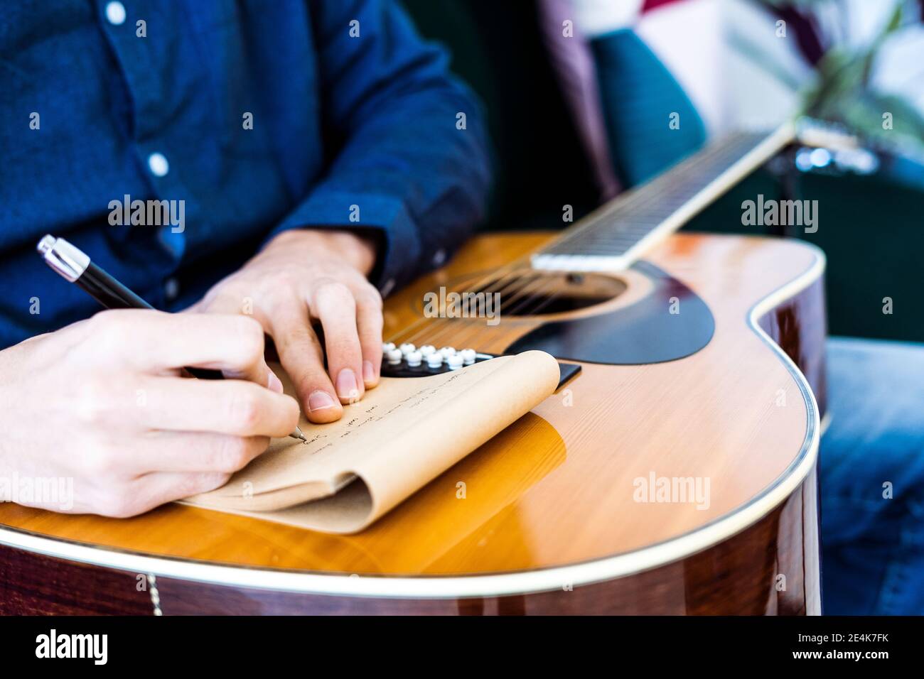 Song writer writing music on note pad while sitting with guitar at studio Stock Photo