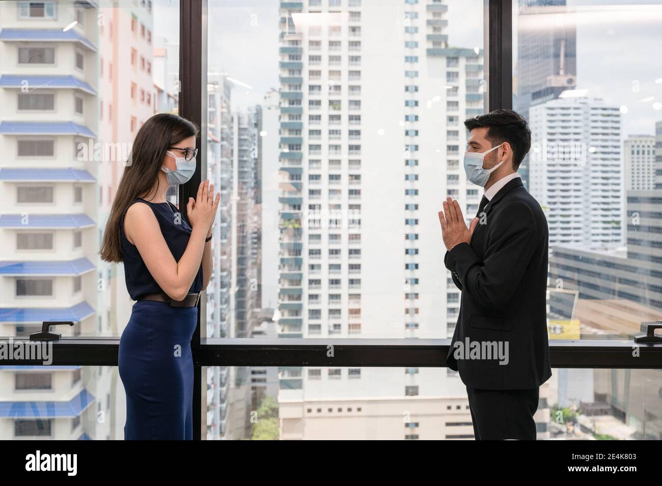 Young caucasian business colleague wearing face mask with thai style greeting for social distanting concept in new normal office at downtown Stock Photo