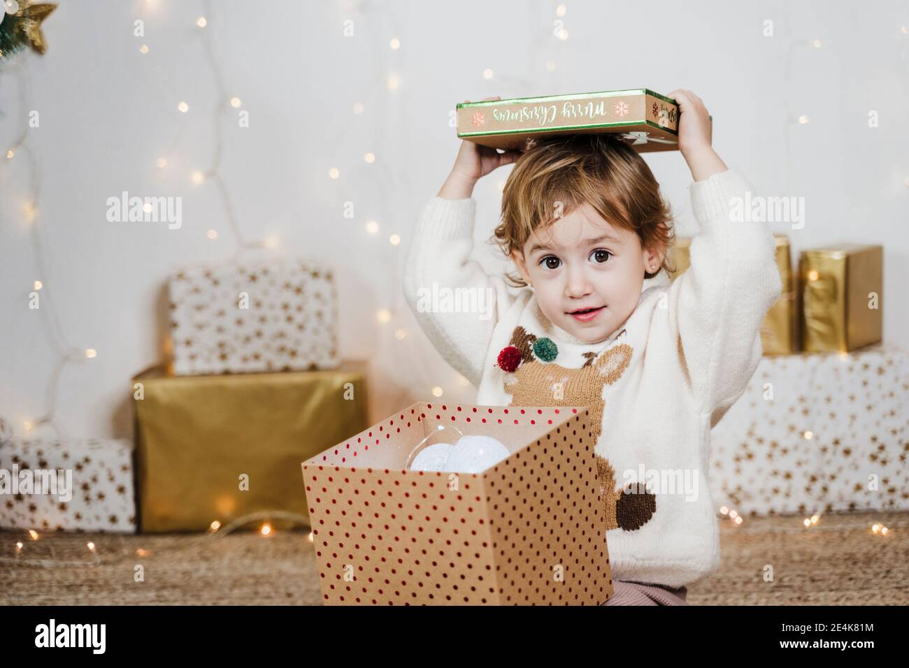 Cute baby girl opening Christmas present while sitting at home Stock Photo