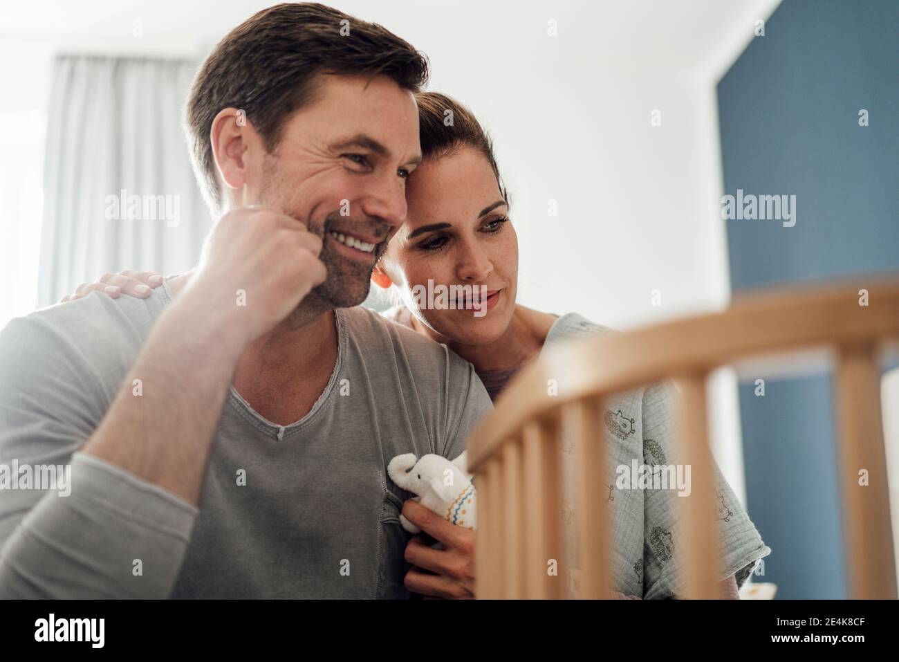 Happy mature couple with stuffed elephant toy looking at crib in bedroom Stock Photo