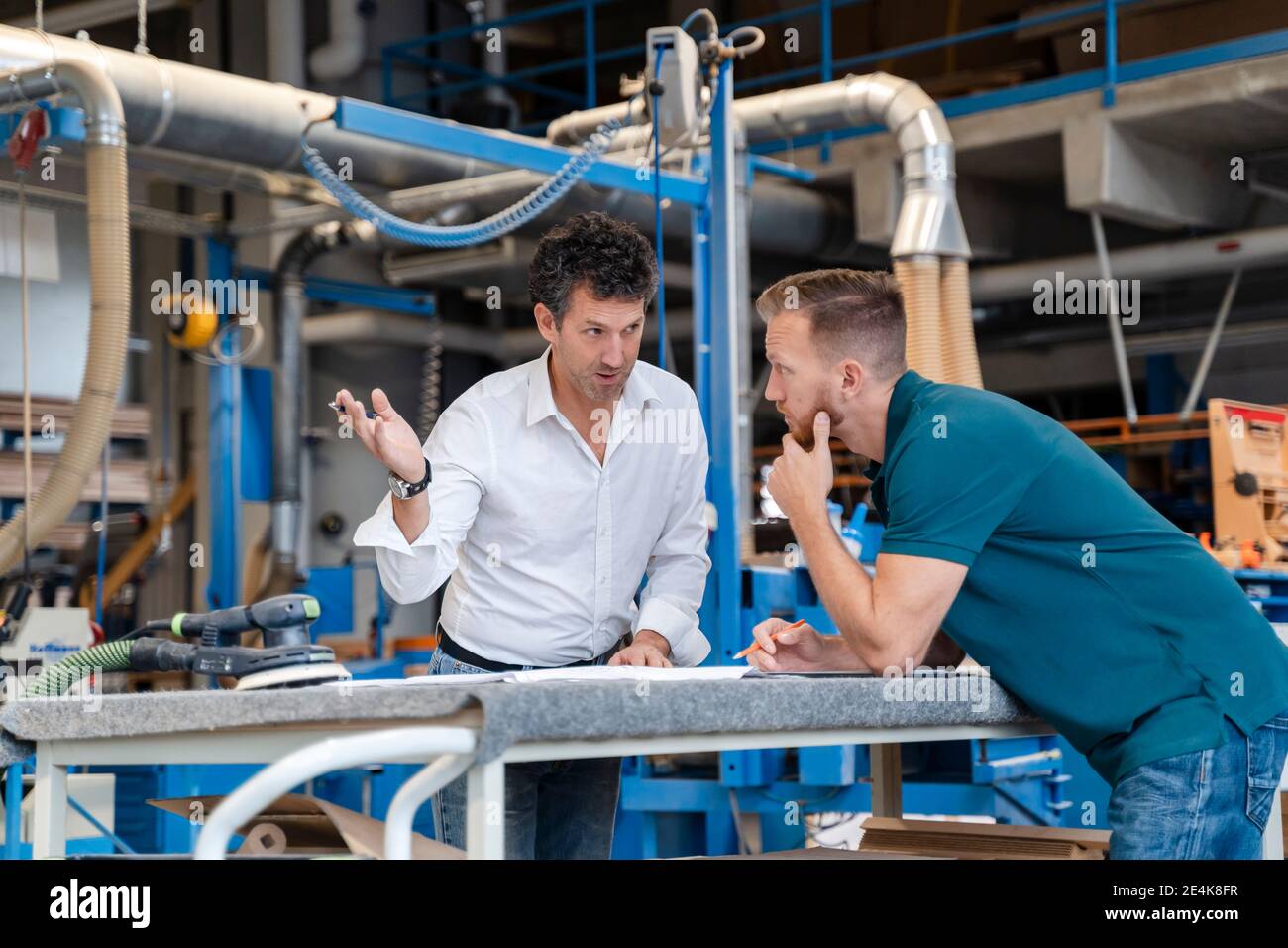Two carpenters talking over documents in production hall Stock Photo