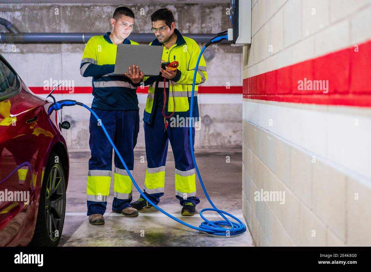 Male technicians using laptop while charging electric vehicle in auto