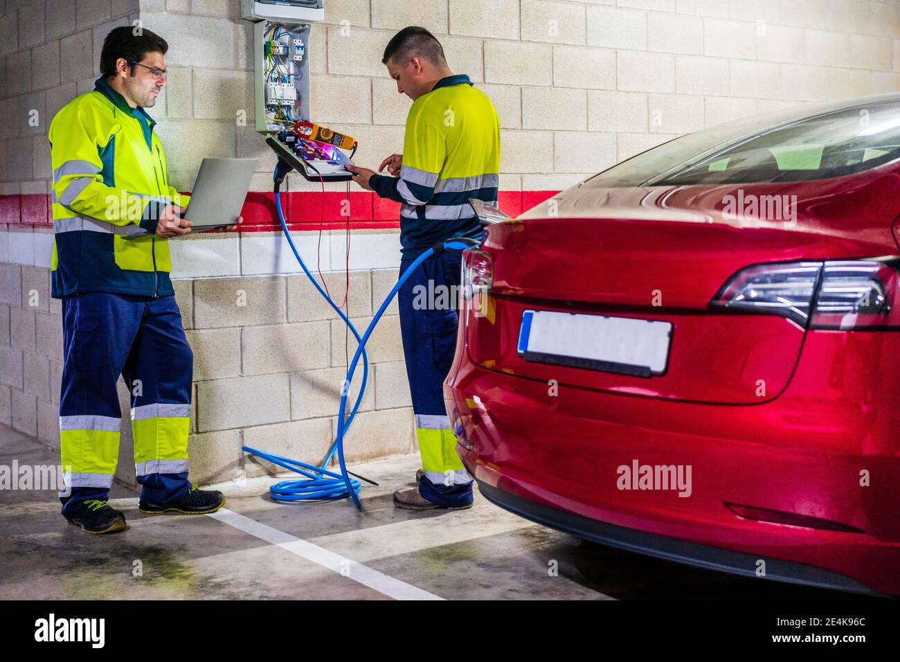 Male technicians working by meter while charging electric car in auto