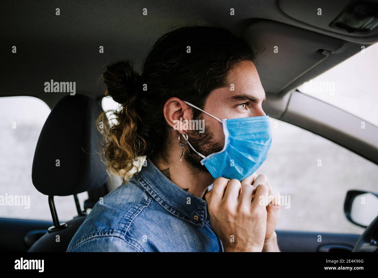 Stylish young man adjusting protective face mask in car Stock Photo