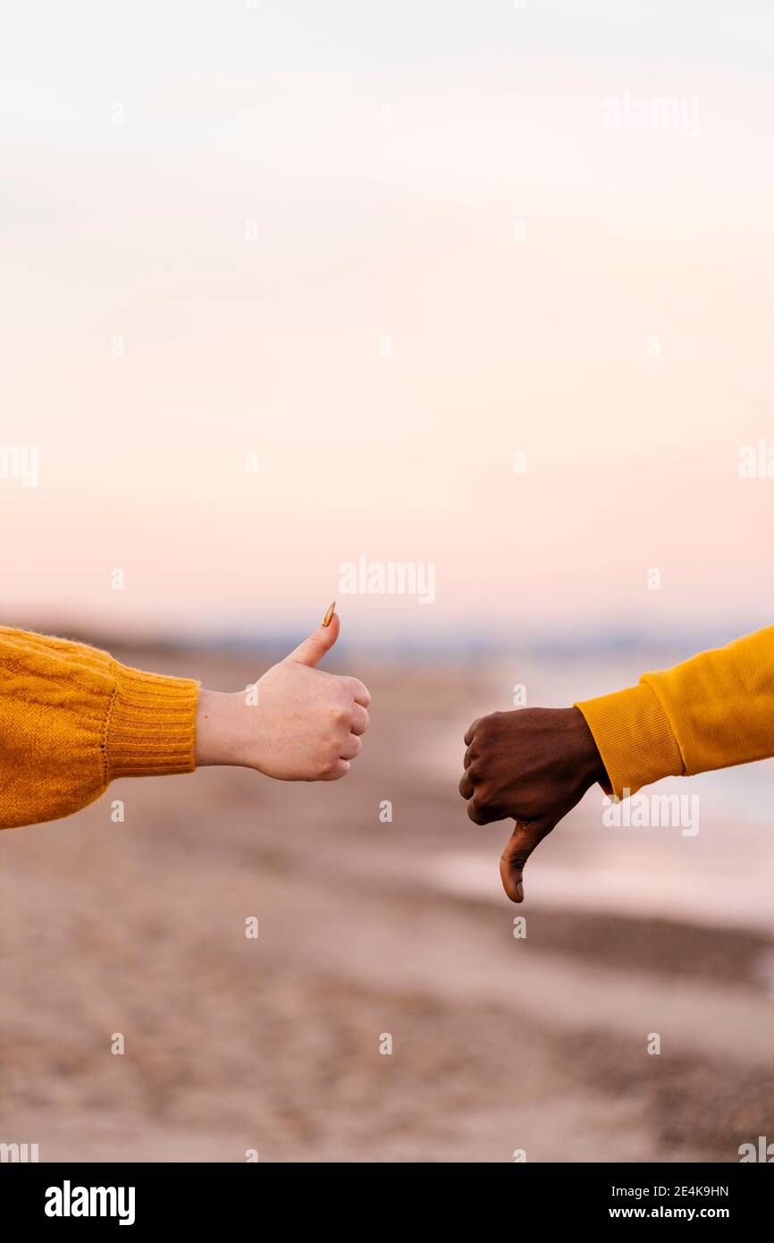 Couple showing thumps up and down gesture at beach Stock Photo
