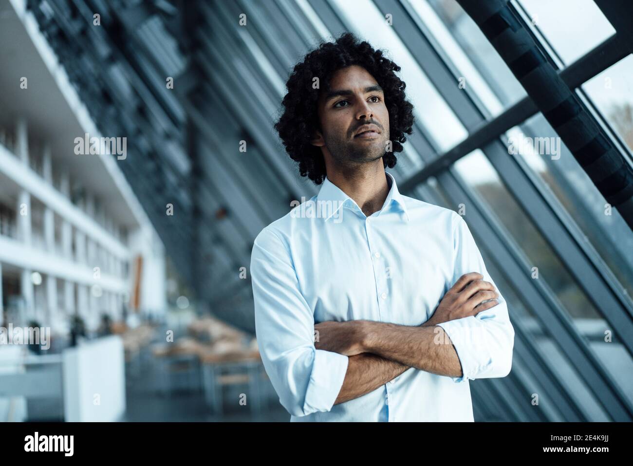 Thoughtful young businessman standing with arms crossed while looking ...