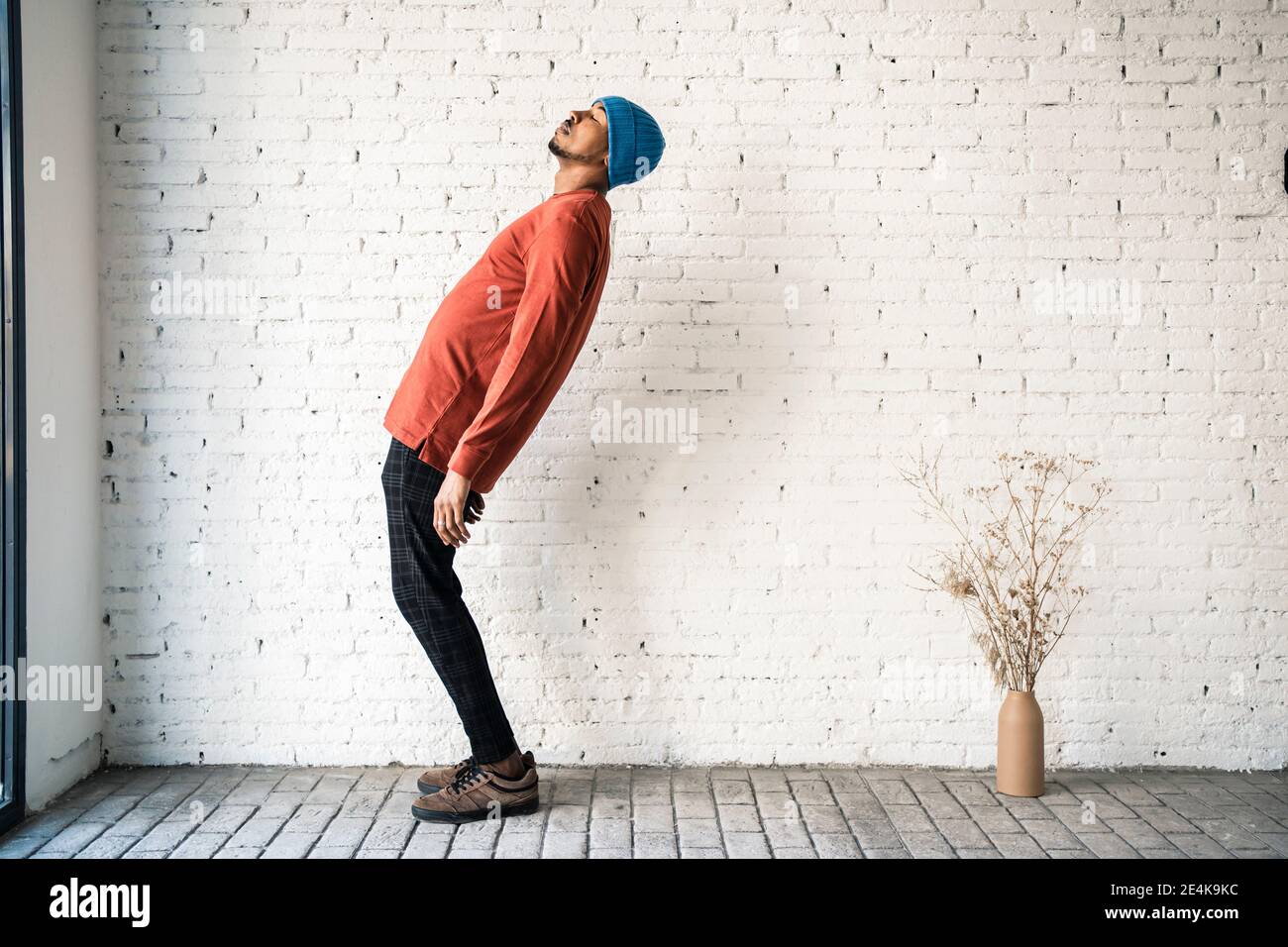 Man with eyes closed bending backwards against white brick wall Stock Photo