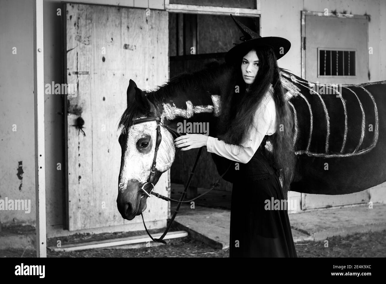 Black and white portrait of a girl in a witch costume with a horse on which a skeleton is drawn Stock Photo