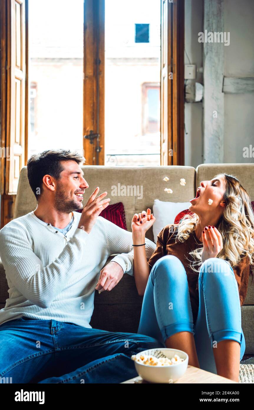 Cheerful young couple sitting at home and playing with popcorn Stock Photo