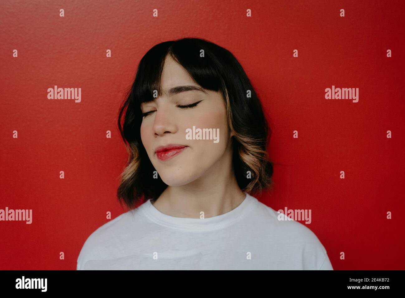 Beautiful woman with eyes closed against red background Stock Photo