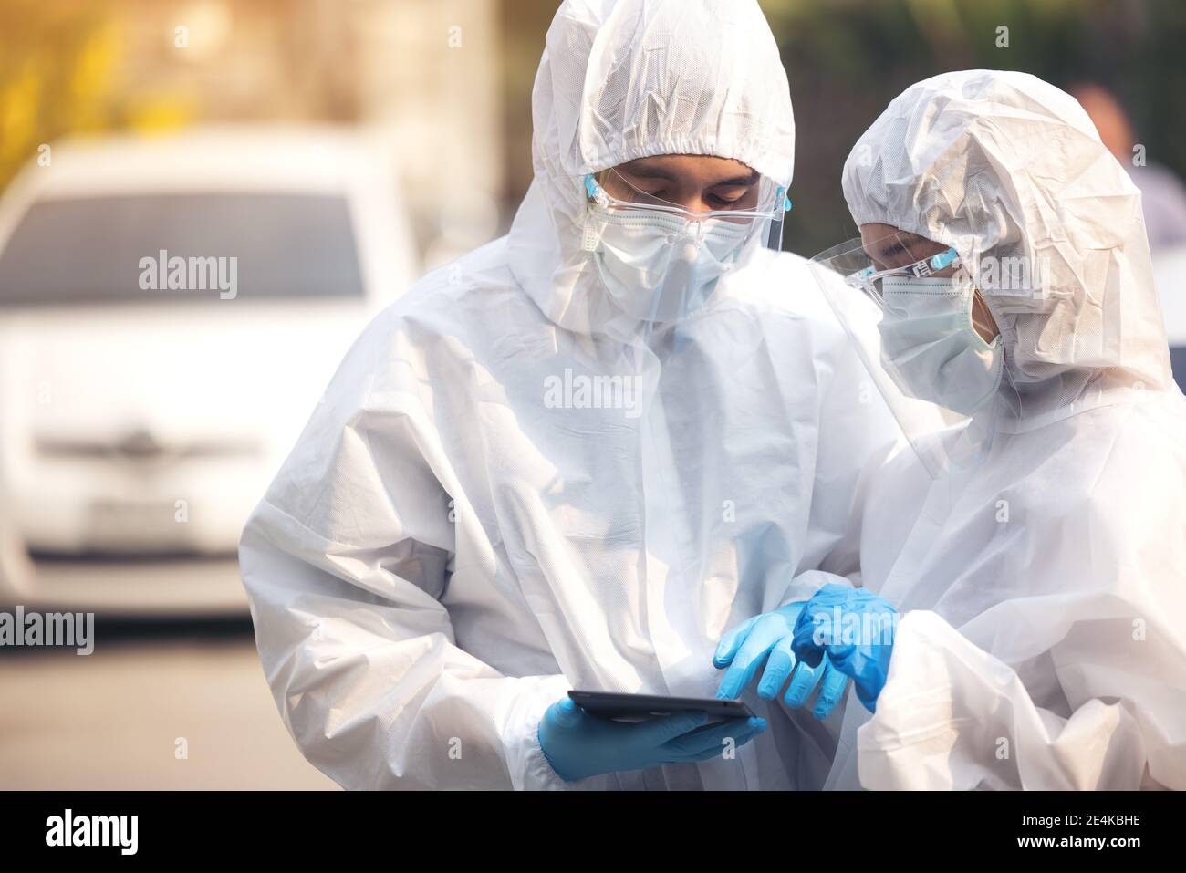 Doctors in ppe suit using tablet with face shield discussing standing on street Stock Photo