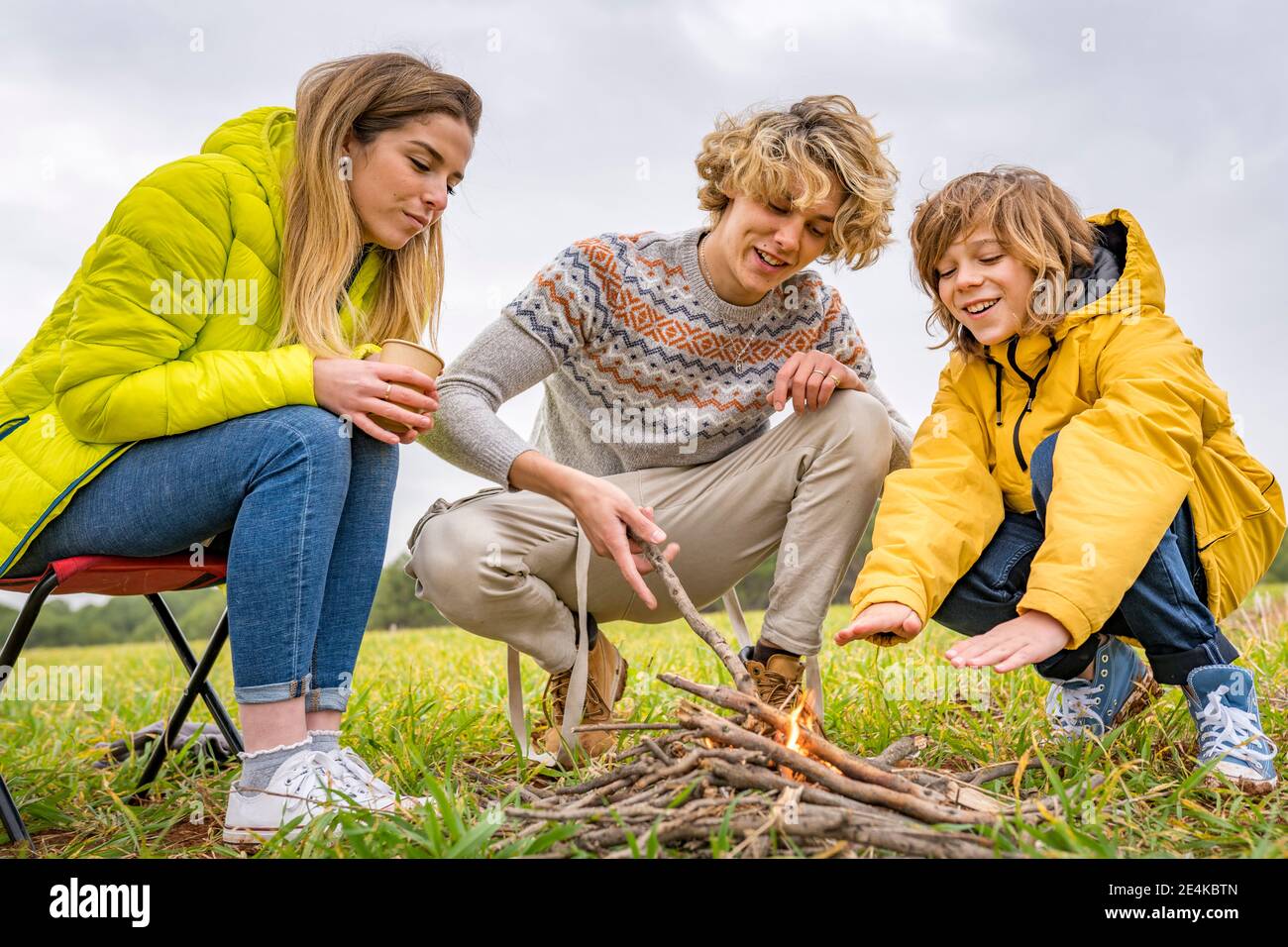 Three siblings starting campfire in grassy field Stock Photo