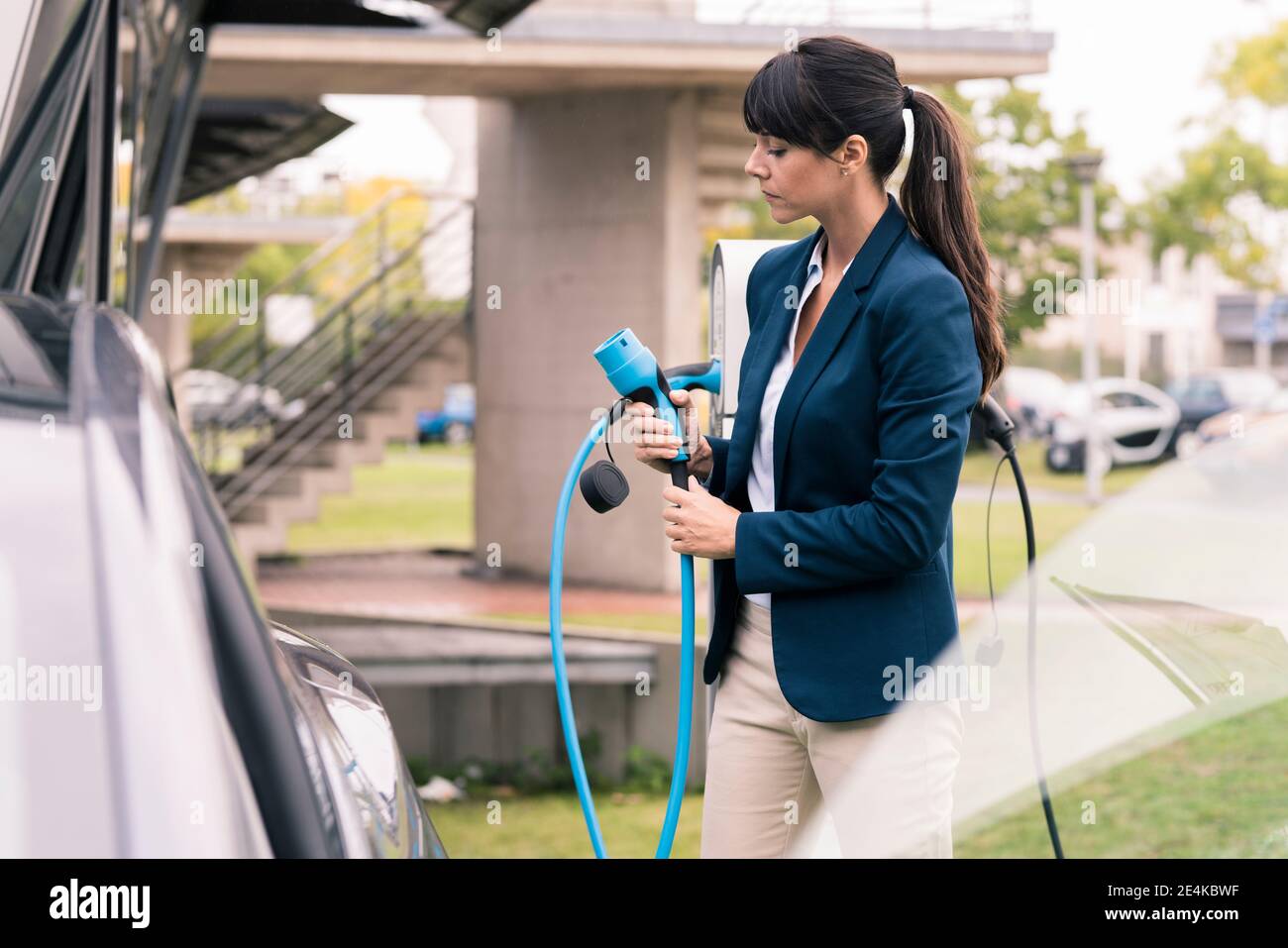 Businesswoman holding electric car charger at station Stock Photo