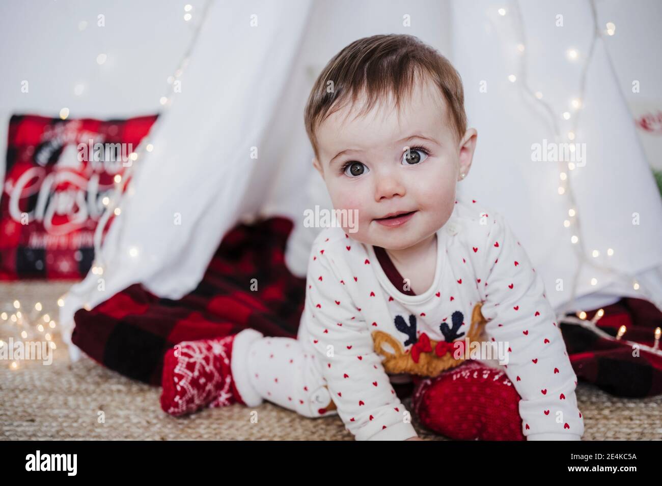 Cute baby girl smiling while sitting against tent during Christmas at home Stock Photo