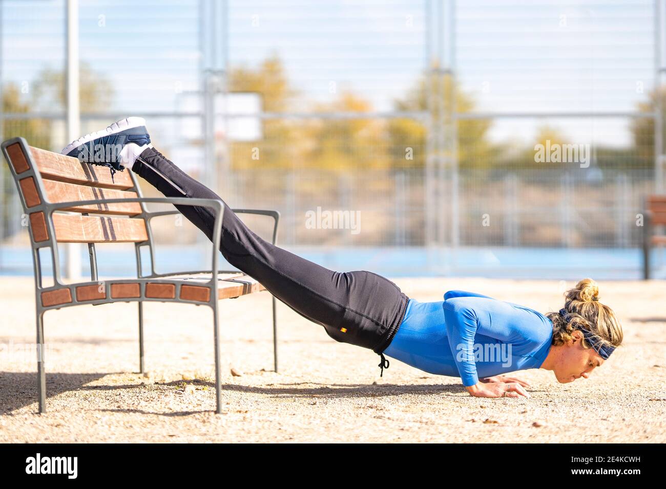 Male runner doing push ups with dedication on bench in public park on sunny day Stock Photo