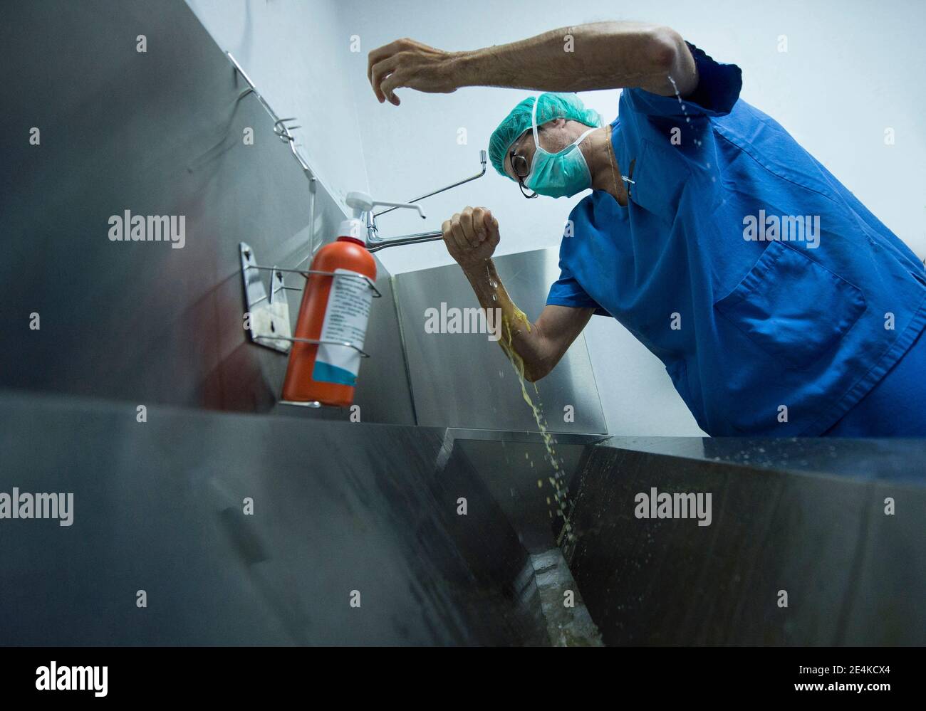 Male doctor scrubbing hands by sink at hospital Stock Photo