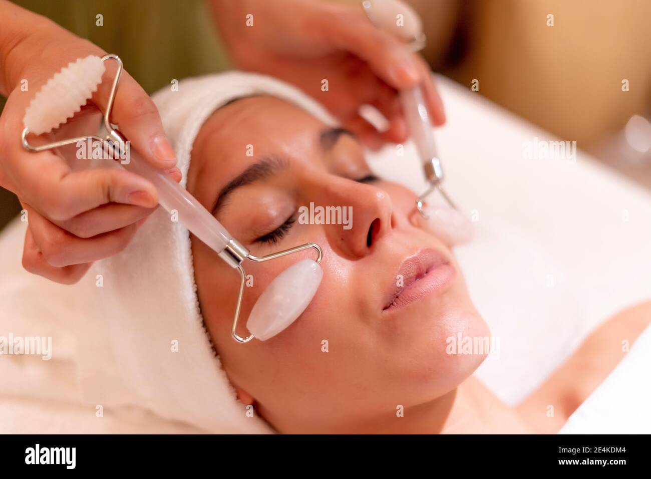 Young female customer receiving facial massage during treatment from beautician at spa Stock Photo